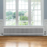 Traditionell vit 4-kolonnsradiator i metall, 300 x 1505 mm, placerad under ett stort fönster med trädetaljer och parkettgolv