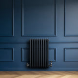 Traditionell antracitgrå 4-kolonnsradiator med släta ytor och rörliga ventiler, placerad mot en mörkblå vägg