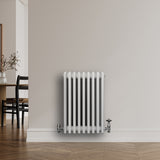 Traditionell vit 4-kolonnsradiator med släta ytor, placerad på en ljus vägg, kompletterad med metallventiler och golvplatta