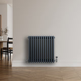 Traditionell antracitgrå 4-kolonnsradiator med släta ytor och ventiler, placerad mot en ljus vägg i ett modernt rum
