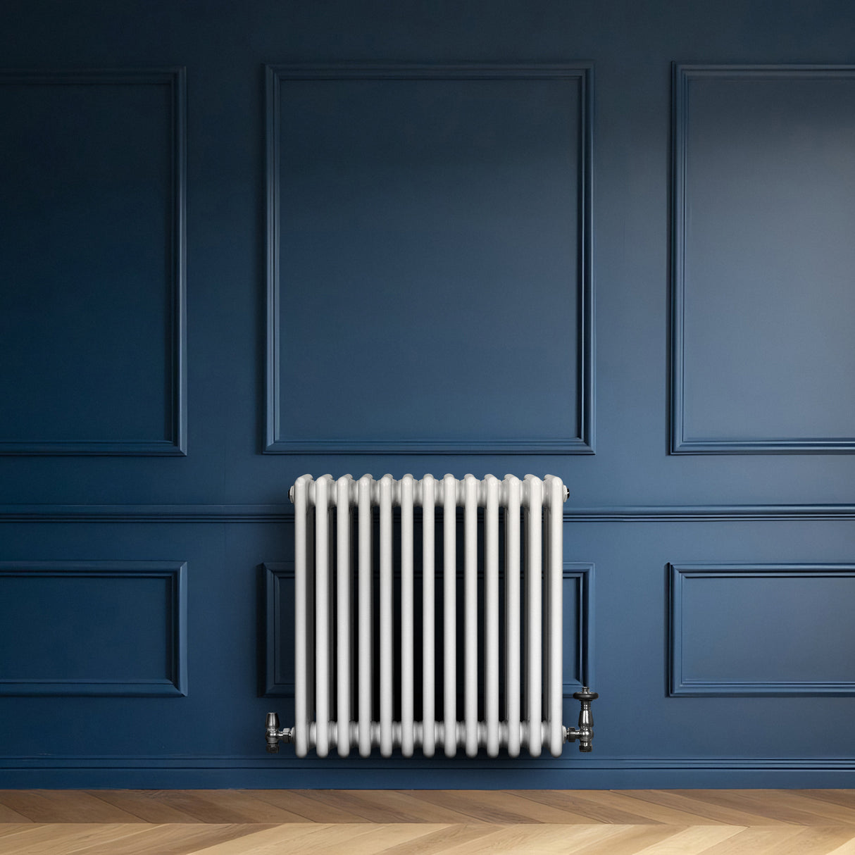 Traditionell vit 4-kolonnsradiator med släta ytor, placerad mot en mörkblå vägg, kompletterad med metallventiler och träparkettgolv
