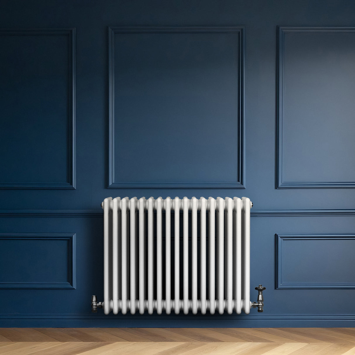 Traditionell vit 4-kolonnsradiator med släta ytor, placerad mot en mörkblå vägg, kompletterad med ventiler och träparkettgolv