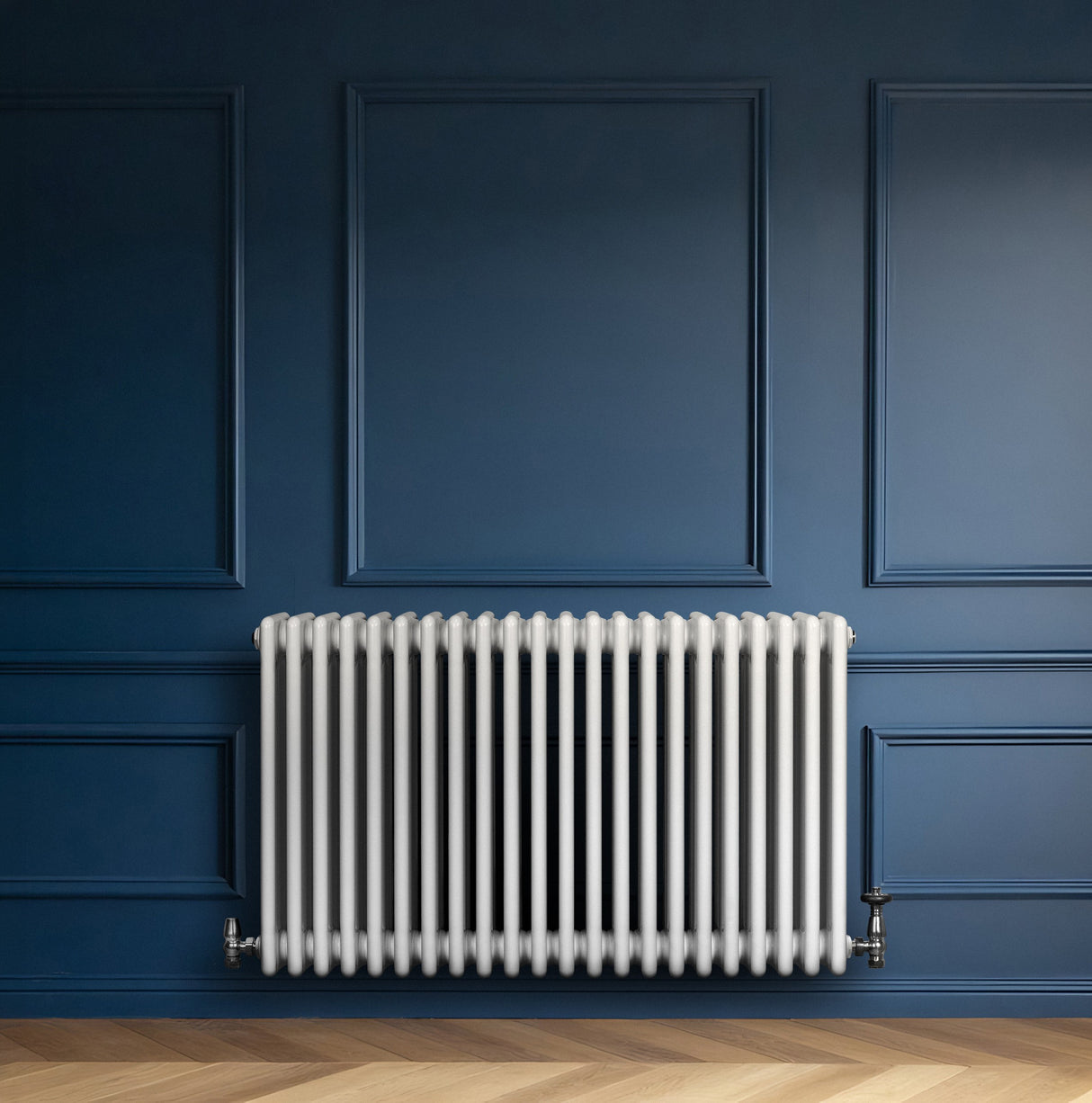 Traditionell vit 4-kolonnsradiator i metall, placerad mot en mörkblå vägg, med släta, runda rör och eleganta ventiler
