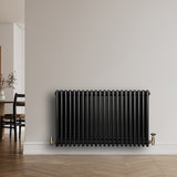 Svart traditionell 4-kolonnsradiator med glänsande yta, placerad mot en ljus vägg, med synliga ventiler i mässing