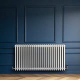 Traditionell vit 4-kolonnsradiator i elegant design, placerad mot en mörkblå vägg, med synliga ventiler och släta ytor