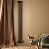 Svart traditionell 4-kolonnsradiator i metall, monterad på vägg, med eleganta ventiler och en varm, neutral väggfärg i bakgrunden