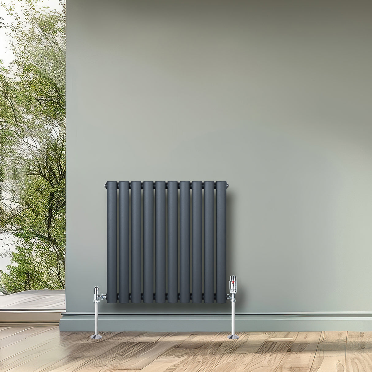 Oval enkelkolonnsradiator i antracitgrå, 600 mm x 600 mm, med glänsande ventiler och stilren design mot en grönskande bakgrund