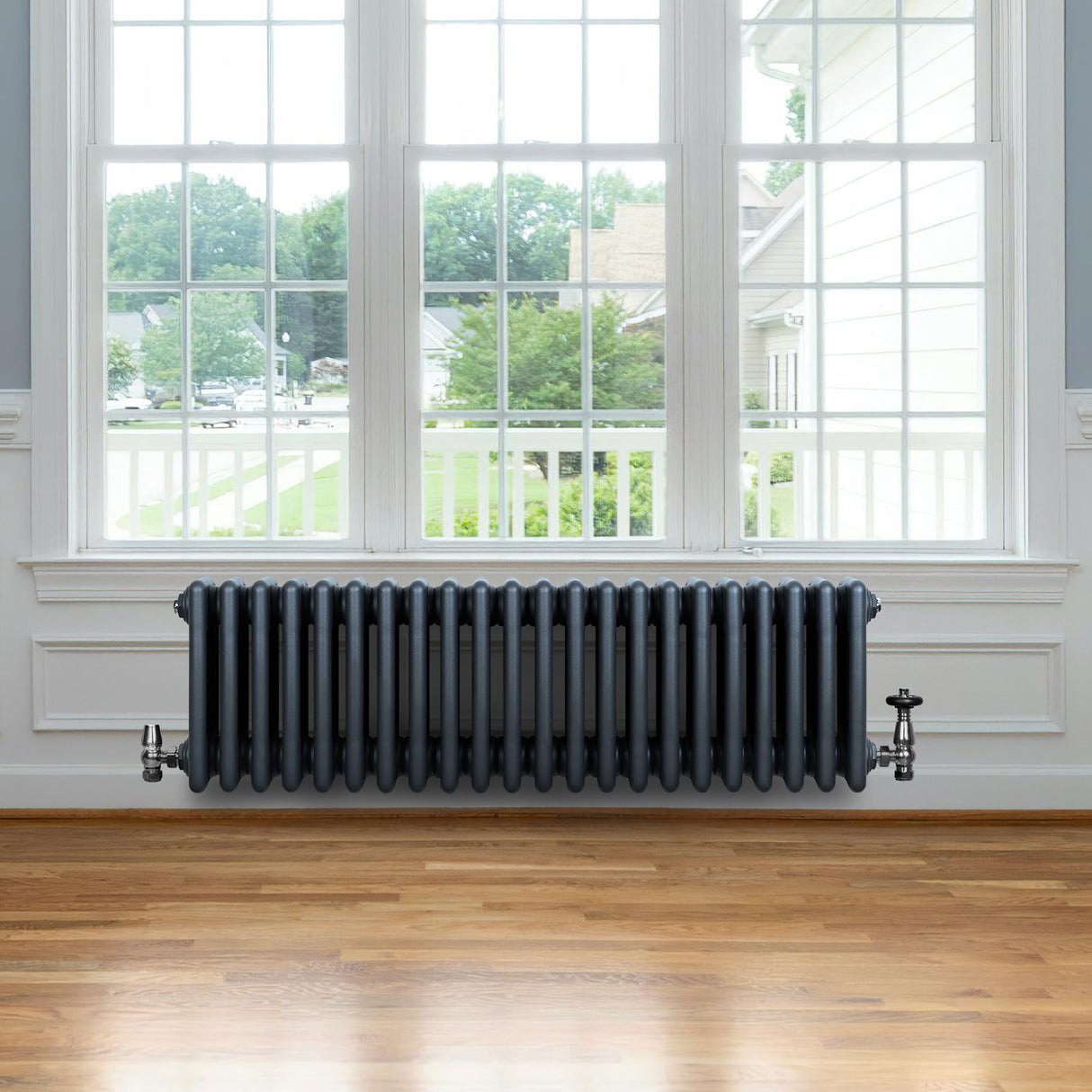 Traditionell 4-kolonnsradiator i antracit med släta, runda sektioner, placerad under ett stort fönster i ett ljust rum