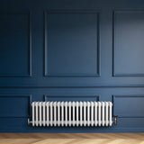 Traditionell vit 4-kolonnsradiator i metall, placerad mot en mörkblå vägg med eleganta paneler och ett ljust trägolv