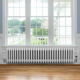 Traditionell vit 4-kolonnsradiator i metall, 300 x 1370 mm, placerad under ett stort fönster med trädetaljer och parkettgolv