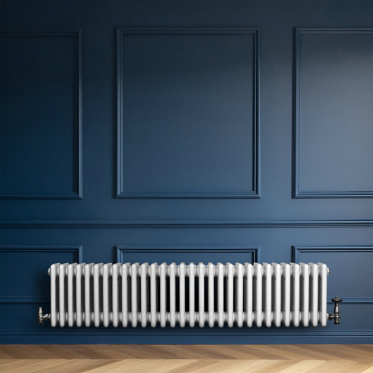 Traditionell vit 4-kolonnsradiator i metall, placerad mot en mörkblå vägg, med en slät och glänsande yta och rundade former