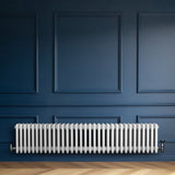 Traditionell vit 4-kolonnsradiator i metall, placerad längs en blå vägg, med släta, rundade former och synliga röranslutningar