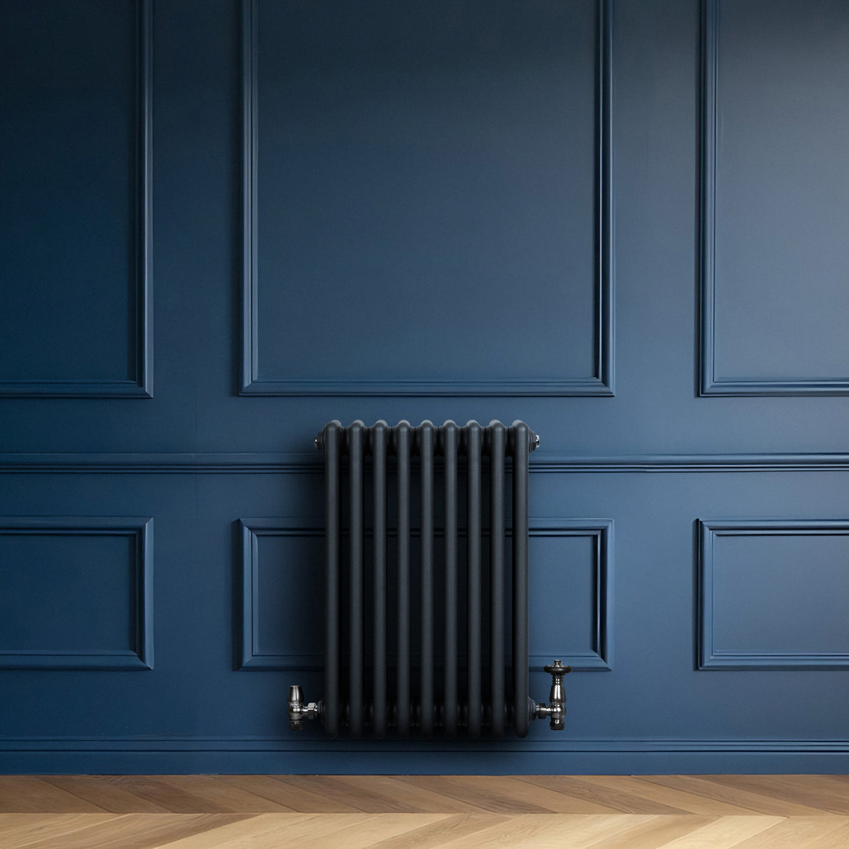 Traditionell 4-kolonnsradiator i antracitgrå, med släta ytor och rundade kanter, monterad på en blå vägg med trädetaljer