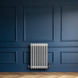 Traditionell vit 4-kolonnsradiator i metall, placerad mot en mörkblå vägg, med släta ytor och eleganta linjer