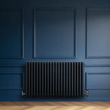 Traditionell 4-kolonnsradiator i antracitgrå, med släta ytor och rundade kanter, placerad mot en mörkblå vägg