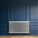 Traditionell vit 4-kolonnsradiator i metall, 600 x 1010 mm, monterad på en blå vägg med träparkettgolv, elegant och stilren design