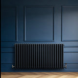 Traditionell 4-kolonnsradiator i antracitgrå med släta, runda rör, installerad mot en mörkblå vägg i elegant inredning