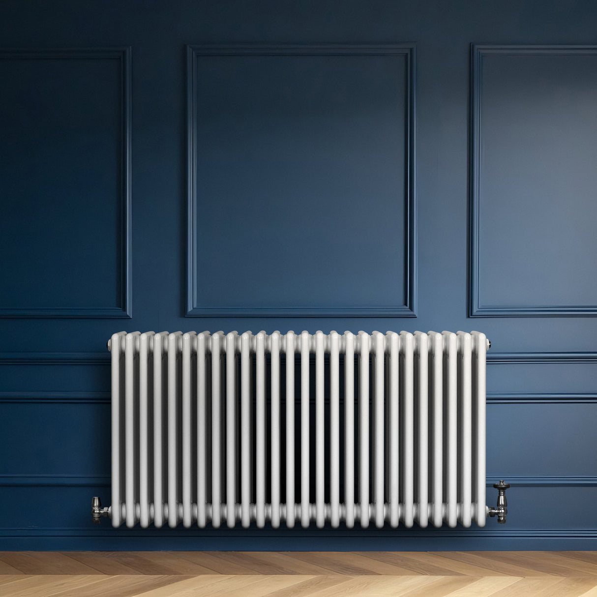 Traditionell vit 4-kolonnsradiator i metall, placerad mot en mörkblå vägg, med släta ytor och eleganta linjer