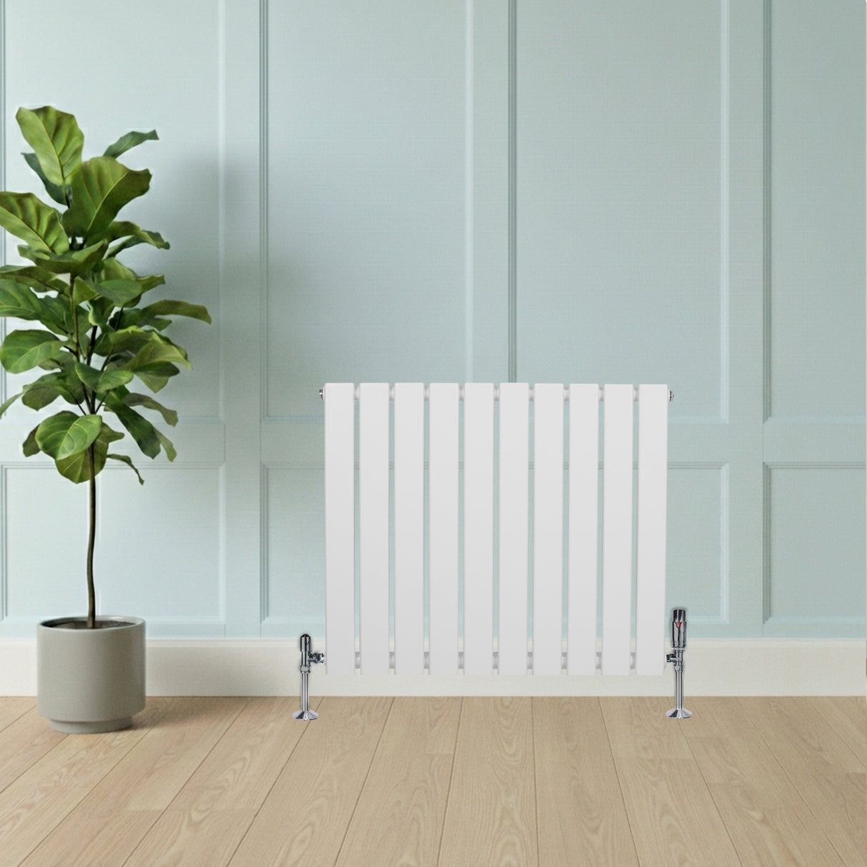 Vit platt enkelpelarradiator med släta ytor och vertikala ribbor, placerad mot en ljusblå vägg med en grön växt i bakgrunden