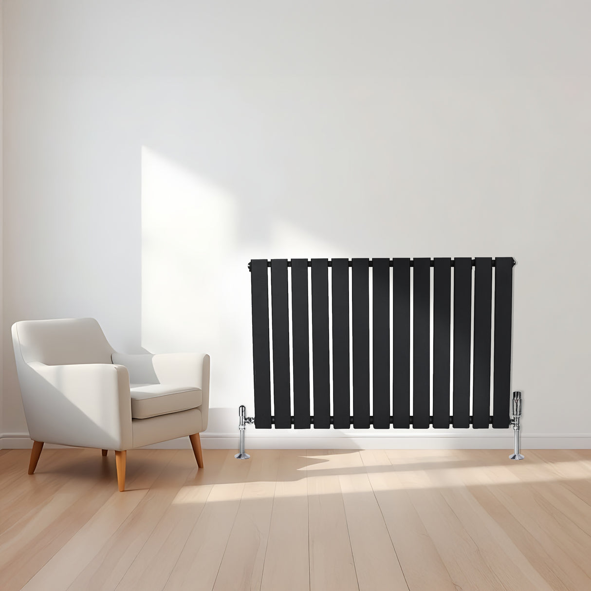 Svart platt enkelpelarradiator med vertikala ribbor, placerad på en ljus träyta bredvid en modern vit fåtölj i ett ljust rum