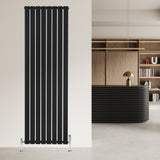 Svart platt enkelpelarradiator med vertikala lameller, monterad på vägg i modern inredning med ljusa färger och stilren design