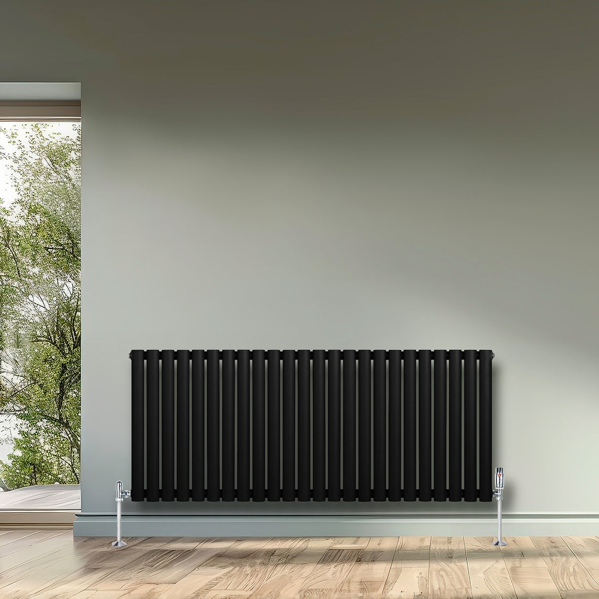 Oval enkelpelarradiator i svart, 600 x 1440 mm, med släta ytor och stilrena linjer, placerad på en ljus vägg i ett rum med trägolv