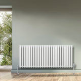 Oval enkelpelarradiator i vit färg, 600 x 1440 mm, med släta ytor och stilren design, placerad mot en grön vägg och fönster