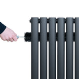 Oval enkelpelarradiator i antracitgrå, rengörs med en borste, visar släta, cylindriska sektioner och modern design
