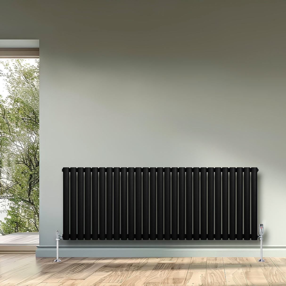 Svart oval enkelpelarradiator med släta ytor, placerad mot en ljus vägg, med träparkett och fönster som släpper in naturligt ljus