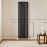 Svart oval enkelpelarradiator i metall, 1800 x 480 mm, monterad på vägg i ett rum med ljusa väggar och trädetaljer
