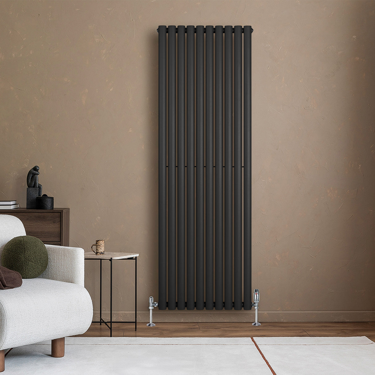Oval enkelpelarradiator i svart, 1800 x 600 mm, med släta ytor och moderna linjer, placerad mot en beige vägg i ett stilrent rum