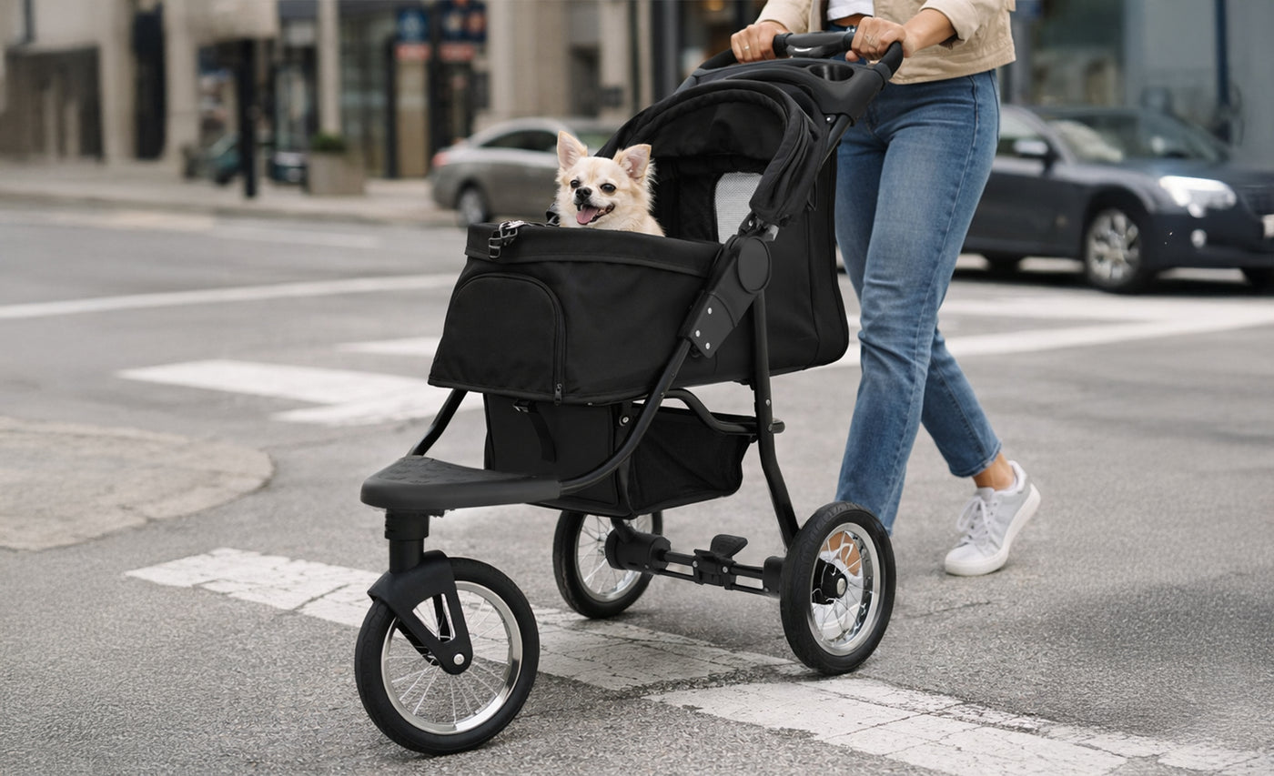 Svart hundvagn med en glad hund inuti, rullande över ett gatan, omgiven av stadsmiljö och bilar i bakgrunden
