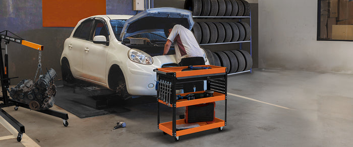 En mekaniker arbetar på en vit bil med öppen motorhuv, en orange verktygsvagn står bredvid med verktyg och delar i en garagemiljö